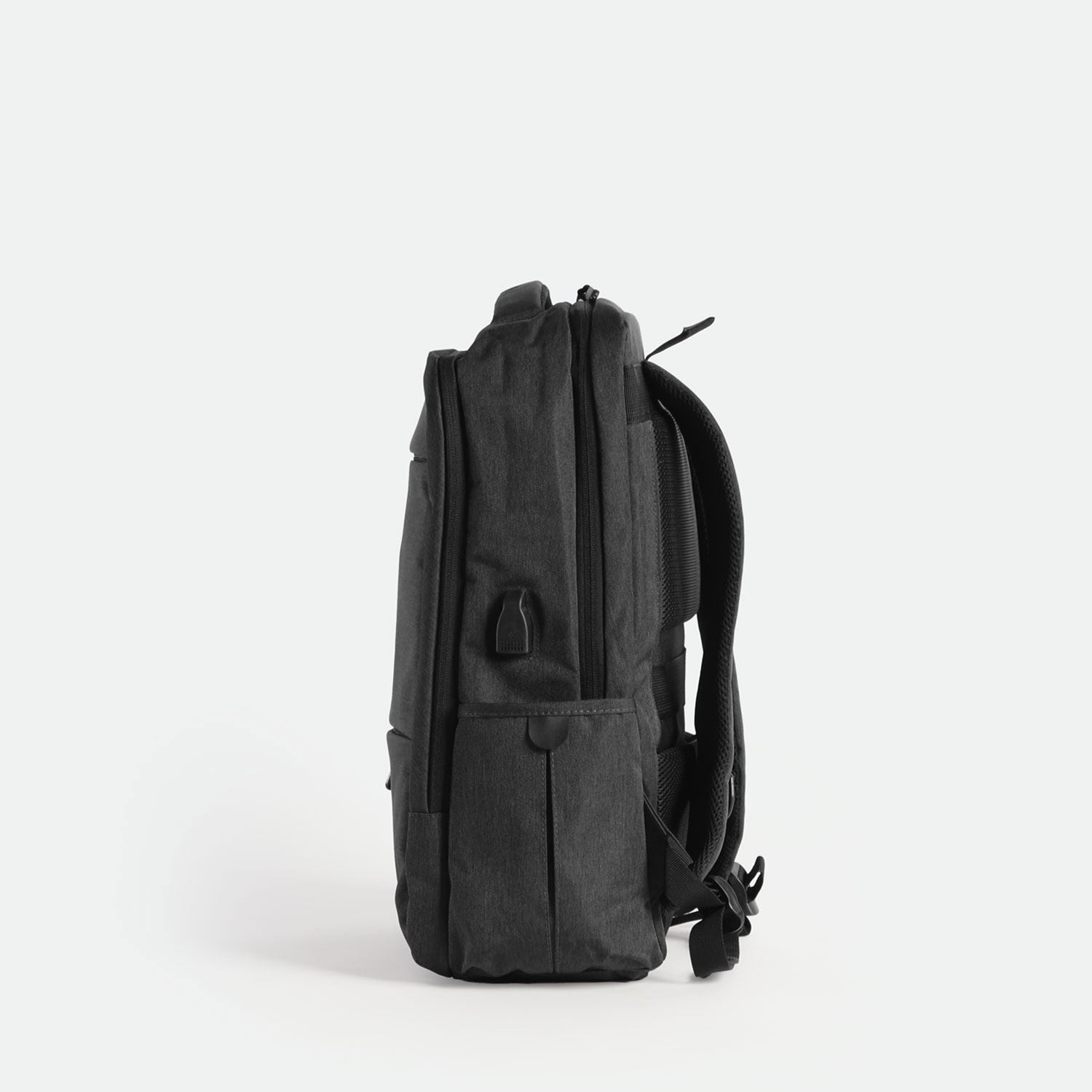 A sleek, iron grey backpack is shown standing upright on its base, viewed from the side against a plain white background. The design is minimalist with subtle zippers and padded shoulder straps visible.