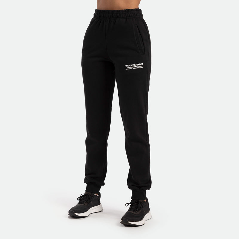a fit woman wearing jogger pant with logo white on front ,she wearing black a athletic shoes ,plus the background is light grey 