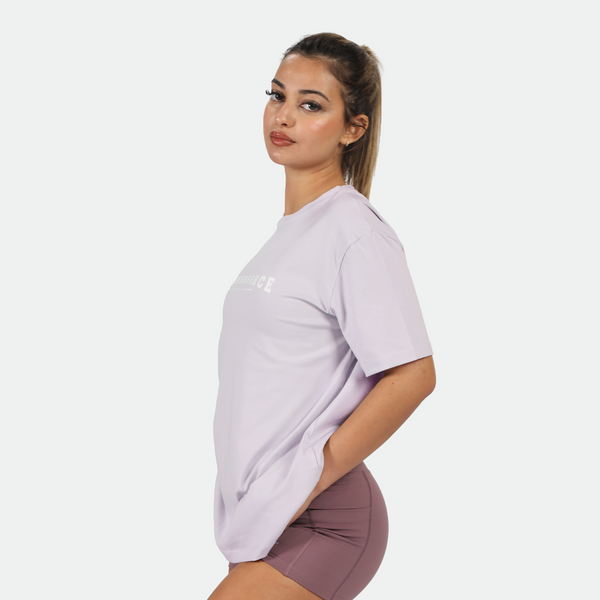 a fit woman stand at right and look at the camera ,she wearing t-shirt lavender blue with short purple 