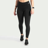 a fit woman wearing legging black  with logo  and shoes black, plus the background is light grey 