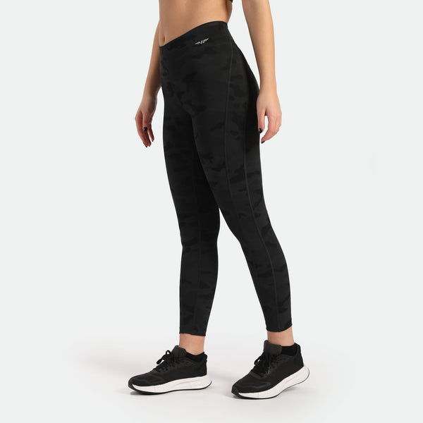 a fit woman stand at the right and wearing camo legging with logo white ,the background is light grey 