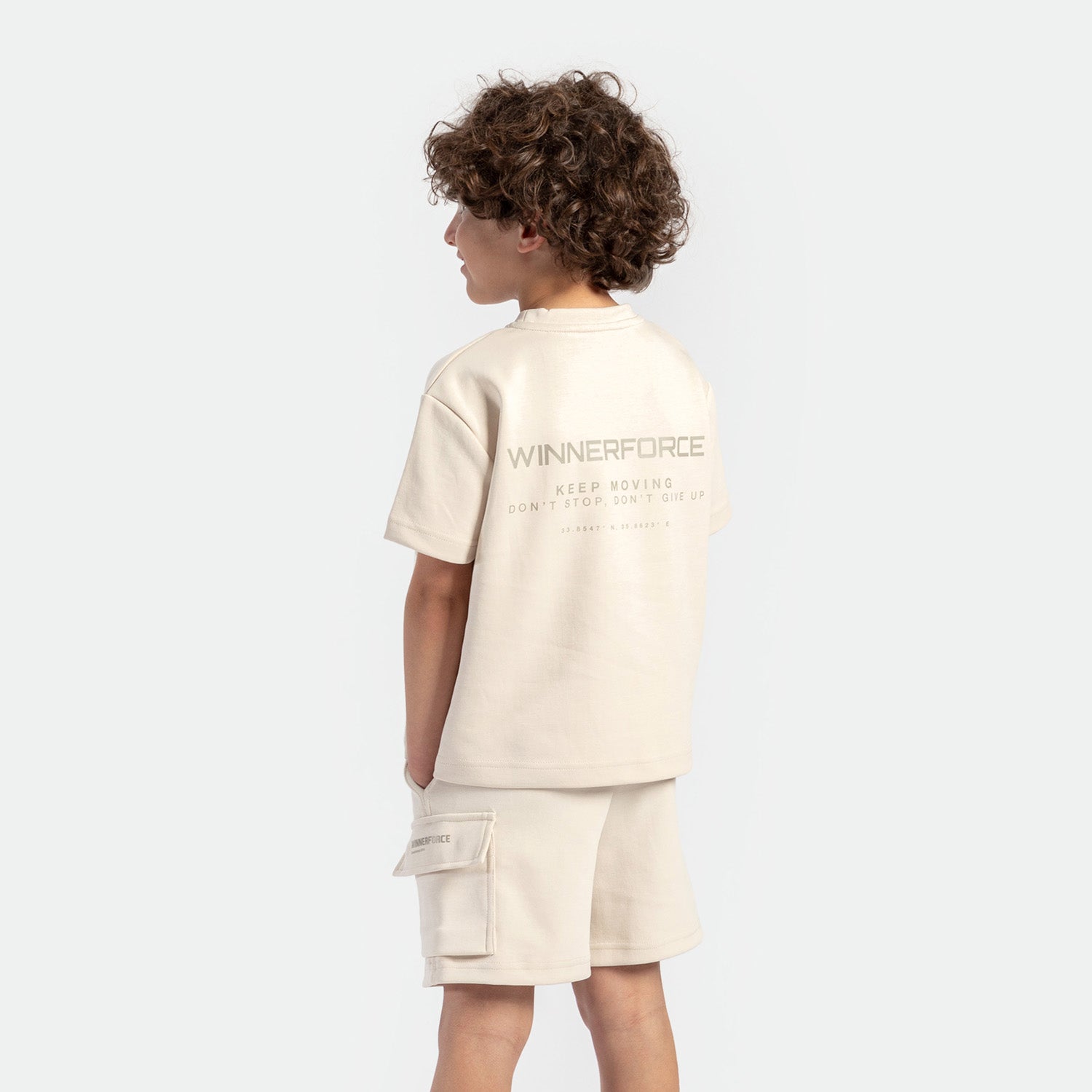 a back view for boy wearing matching set light beige ,t-shirt with logo and short with pocket 