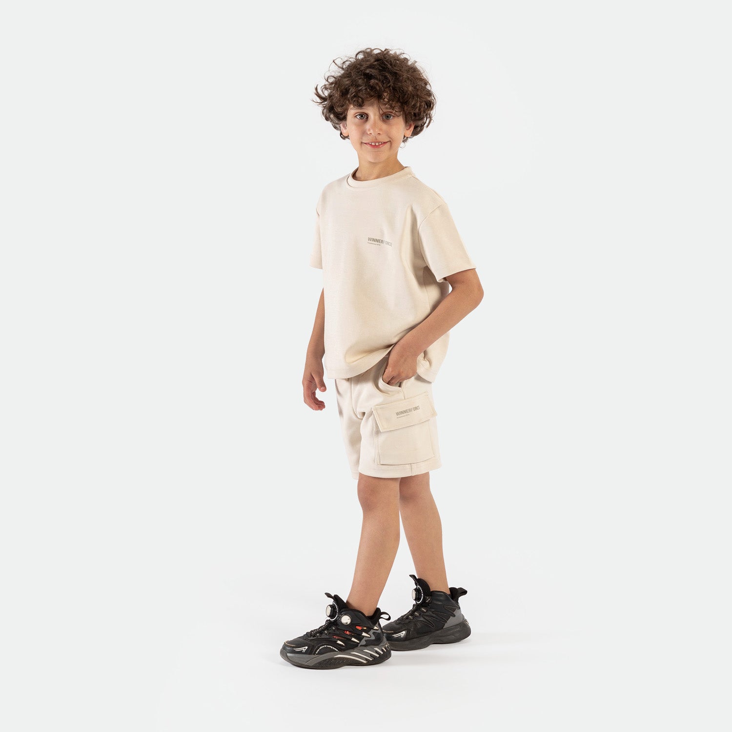 a fit boy stand at right and wearing matching set light beige ,t-shirt and short ,plus the shoes 