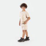 a fit boy stand at right and wearing matching set light beige ,t-shirt and short ,plus the shoes 