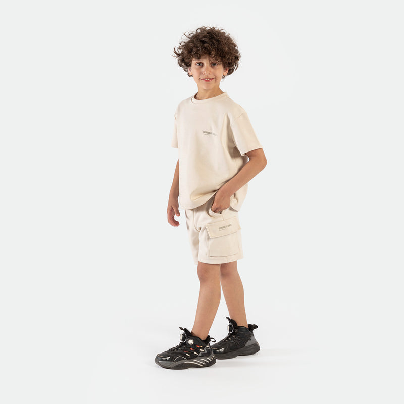 a fit boy stand at right and wearing matching set light beige ,t-shirt and short ,plus the shoes 