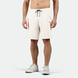 A pair of light beige men's shorts with an elastic waistband, external drawcord, open side pockets, and a zipper on one pocket