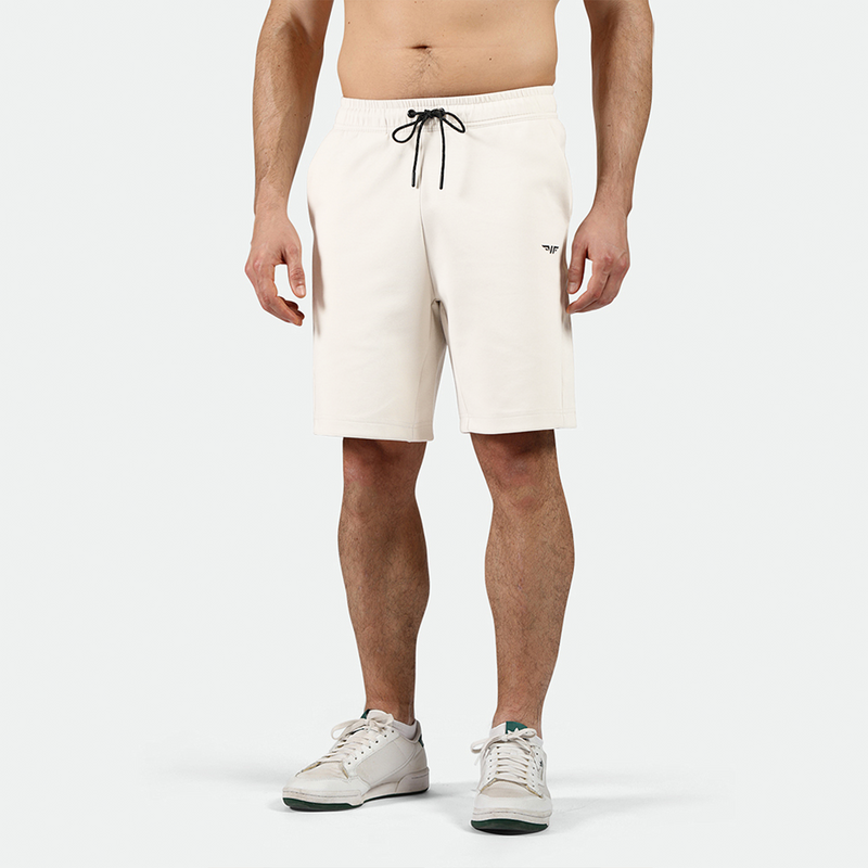 A pair of light beige men's shorts with an elastic waistband, external drawcord, open side pockets, and a zipper on one pocket