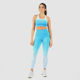 a woman fit wearing matching bra and legging a blue gradien ,she look at the camera ,she wearing shoes white ,plus the background is light grey 