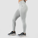  a fit woman stand at right and wearing legging grey with logo black ,she wearing shoes, plus the background is light grey 