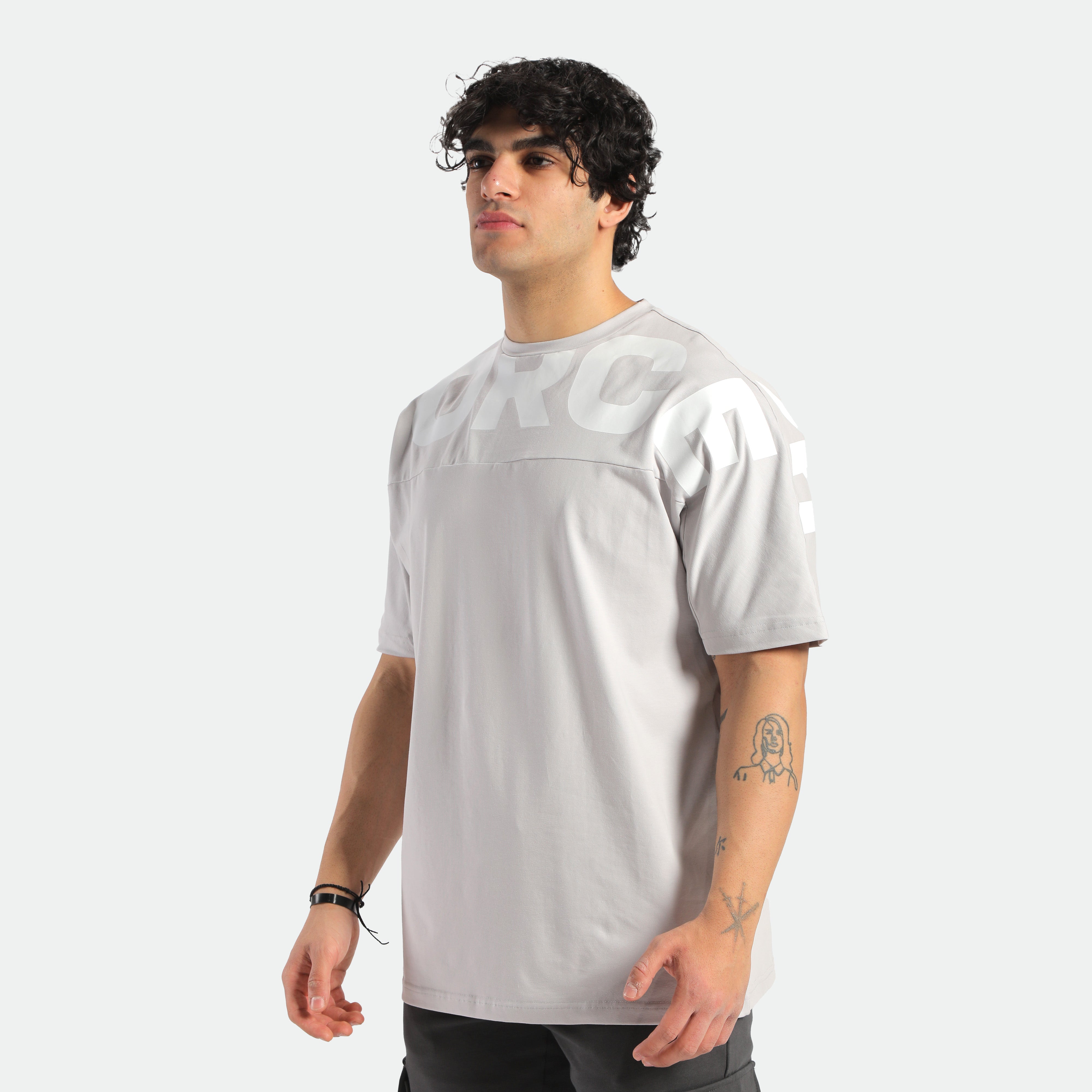 a fit man stand at right and wearing t-shirt light grey with logo ,plus he wearing  pants black 