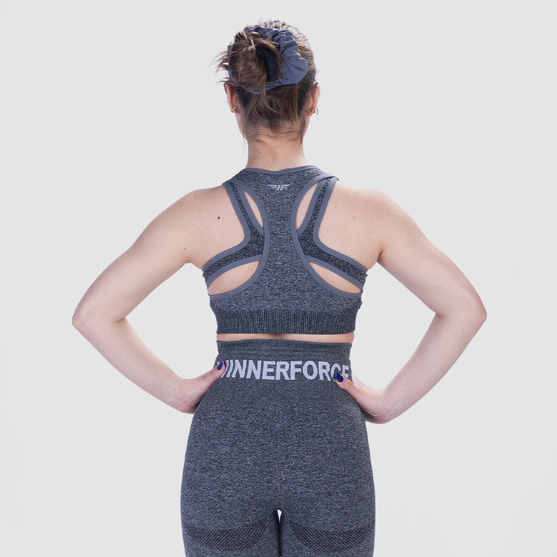A person wearing a gray sports bra and matching leggings is shown from the back. The outfit has a racerback design and the word WINNERFORCE printed on the leggings. The background is plain white