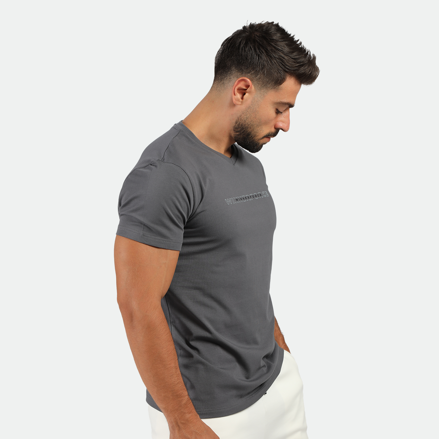 a fit man stand at right and wearing t-shirt mange dark grey with logo and pants white 