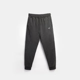 Dark gray jogger pants with an elastic waistband and cuffed ankles, featuring a small logo on the left thigh. The pants are laid flat on a light gray background.