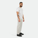 a fit man stand at right  and wearing t-shirt white with pants marl light grey ,plus he wearing shoes black 
