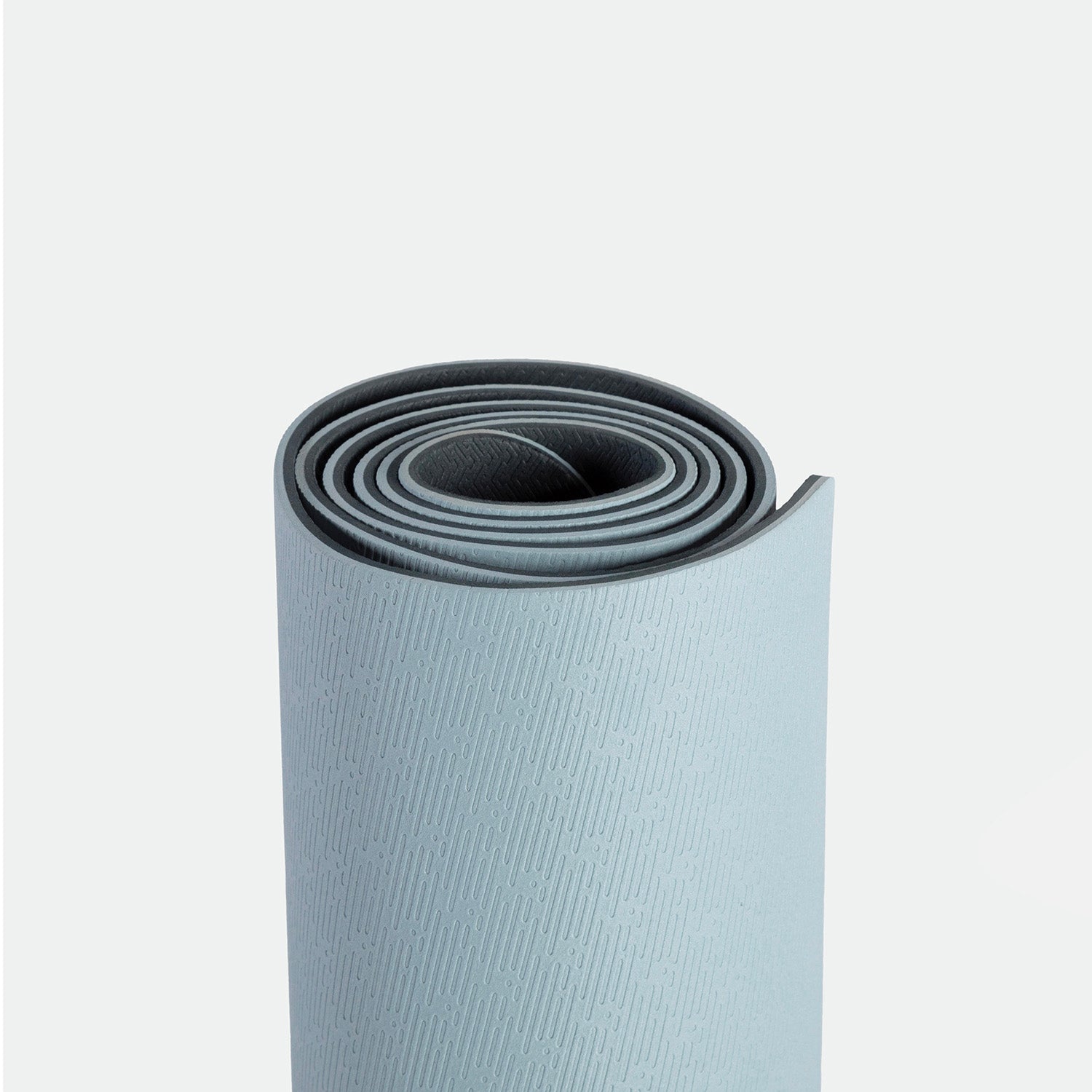 Rolled-up light grey yoga mat with a subtle textured pattern, against a plain white background, suggesting calm and simplicity.