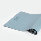 A CHAMBRAY-BLUE yoga mat partially rolled up on a white background. The mat features a central logo with the text "winnerforce," conveying simplicity and calm.