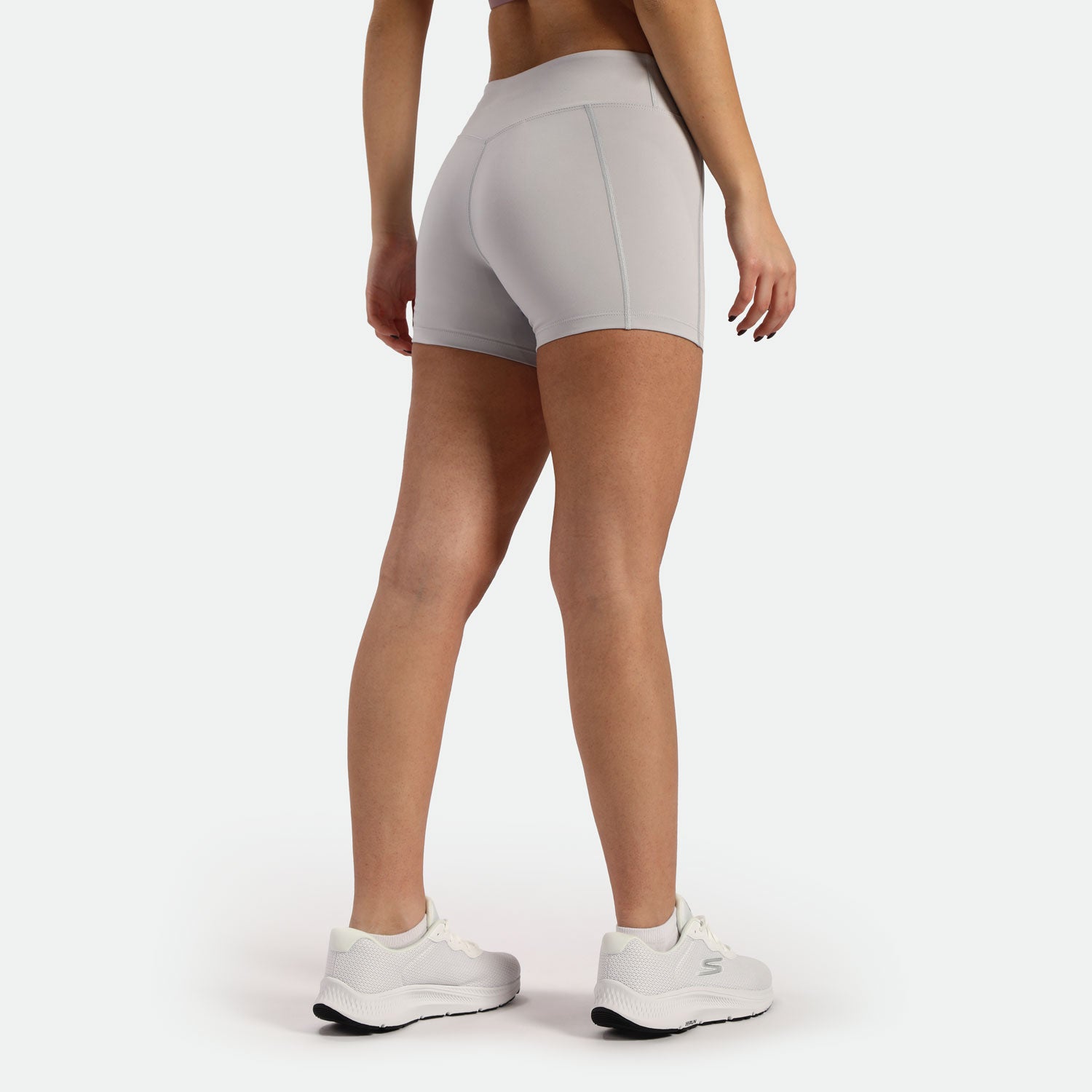 a back view for fit woman wearing short grey and shoes white ,plus the background is light grey  