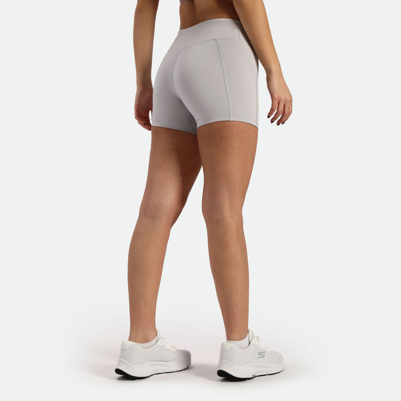 a back view for fit woman wearing short grey and shoes white ,plus the background is light grey  