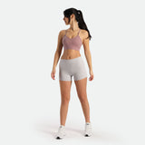 a fit woman stand at right and look at the same direction ,she wearing bra pink and short grey with shoes white ,plus the background is light grey 