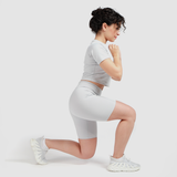 a fit woman stand with exercise sport ,wearing matching set grey, crop top with short ,plus she wearing   sneakers white 