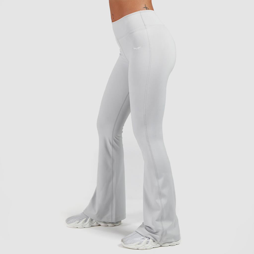a fit woman stand at right and wearing flared legging with shoes white ,the background is light grey 