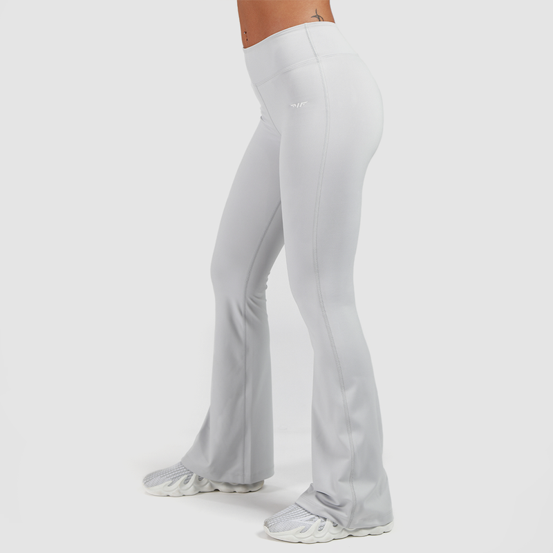 a fit woman stand at right and wearing flared legging with shoes white ,the background is light grey 