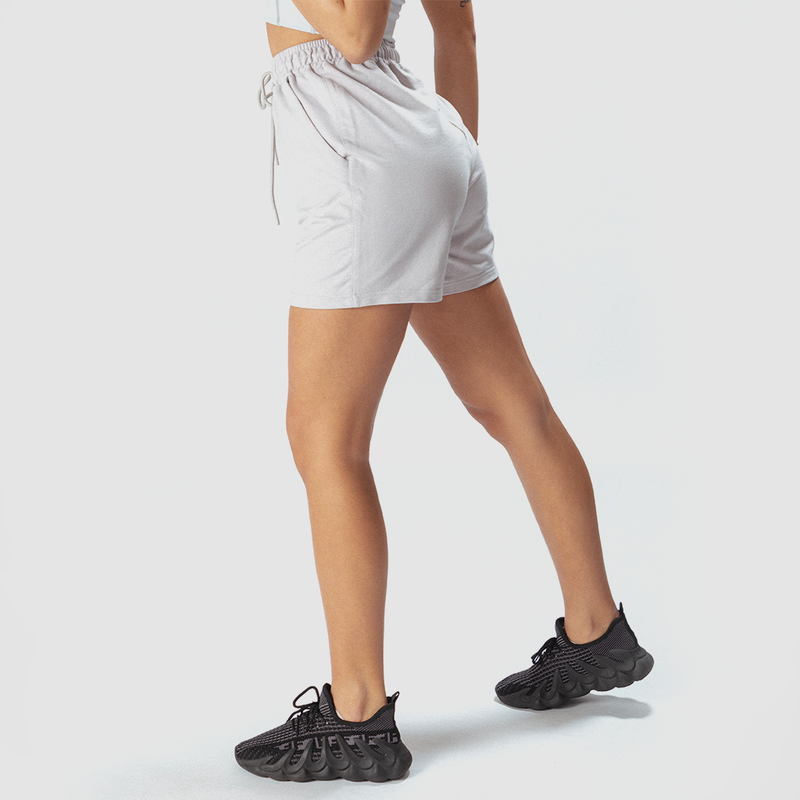 a fit woman stand at right and wearing short grey with shoes black ,plus the background is light grey 