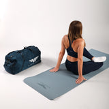 Woman sitting on a yoga mat with a blue duffel bag next to her on a white background