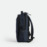 A sleek, navy blue  backpack is shown standing upright on its base, viewed from the side against a plain white background. The design is minimalist with subtle zippers and padded shoulder straps visible.