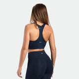 a back view for fit woman wearing matching set navy blue terrazzo, bra and legging plus the logo in half 