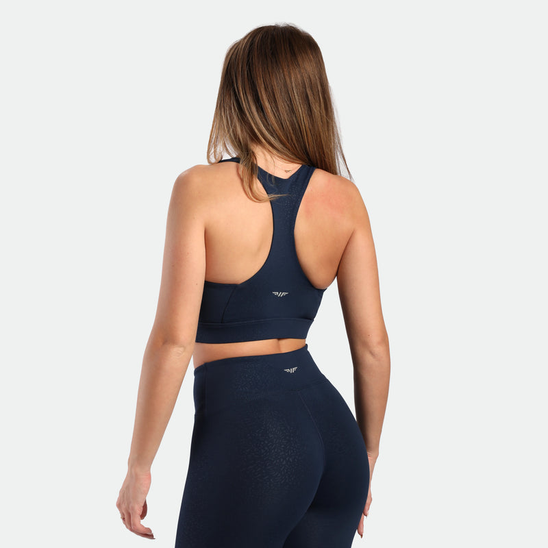 a back view for fit woman wearing matching set navy blue terrazzo, bra and legging plus the logo in half 