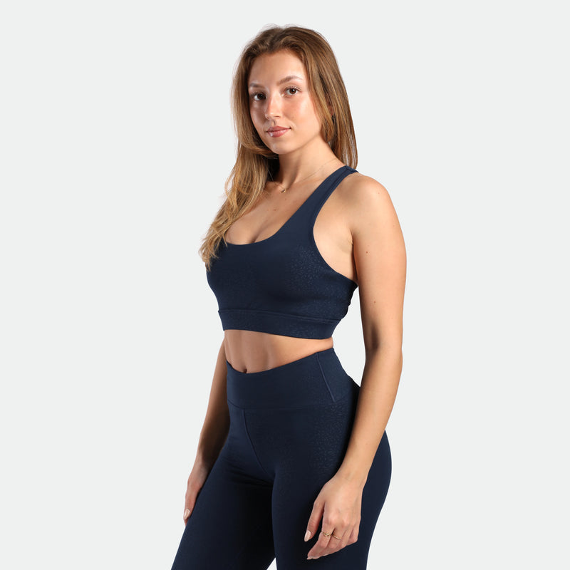a fit woman stand at right  and wearing matching set navy blue terrazzo ,bra and legging 