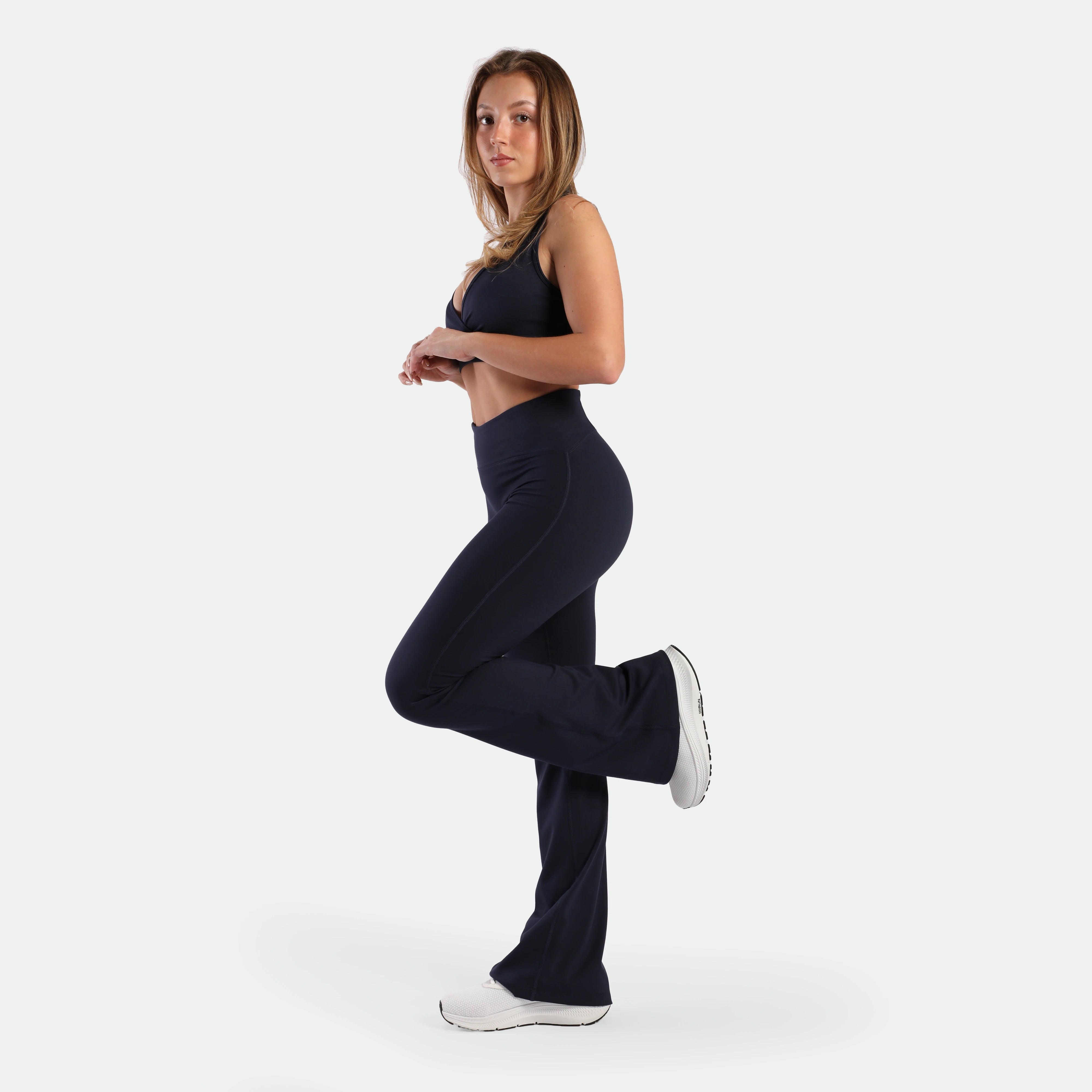 a fit woman stand at right with pose and wearing matching set navy ,bra and legging ,plus the shoes white 