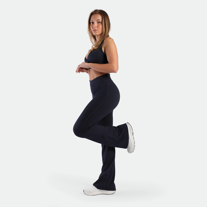 a fit woman stand at right with pose and wearing matching set navy ,bra and legging ,plus the shoes white 