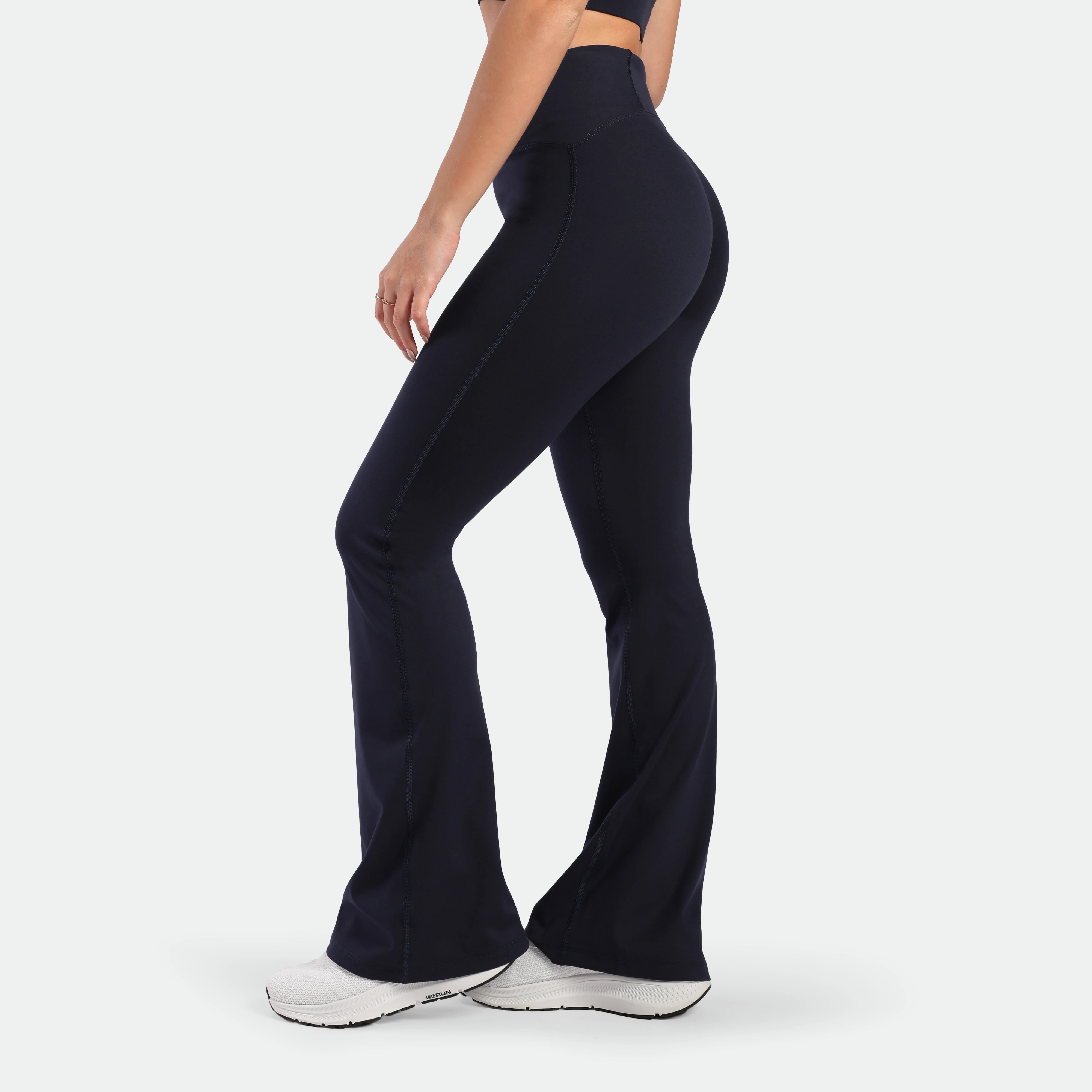 a fit woman stand at right and wearing flared legging navy with shoes white 