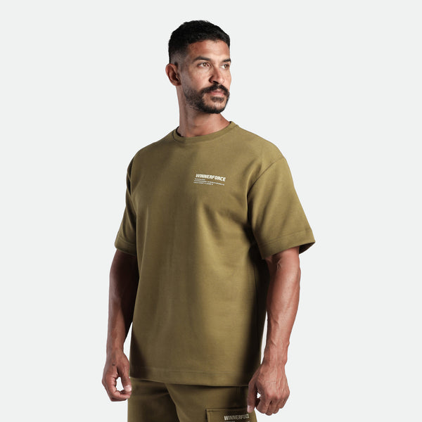 a fit man stand with pose and look at right ,he wearing matching set olive drop t-shirt and short 