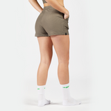 a fit woman stand at right and wearing short olive grey ,plus the background is light grey 