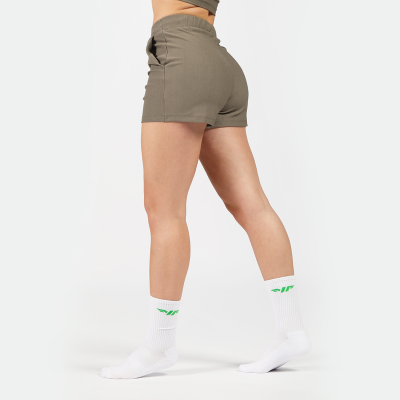 a fit woman stand at right and wearing short olive -grey with socks white ,plus the background is light grey 