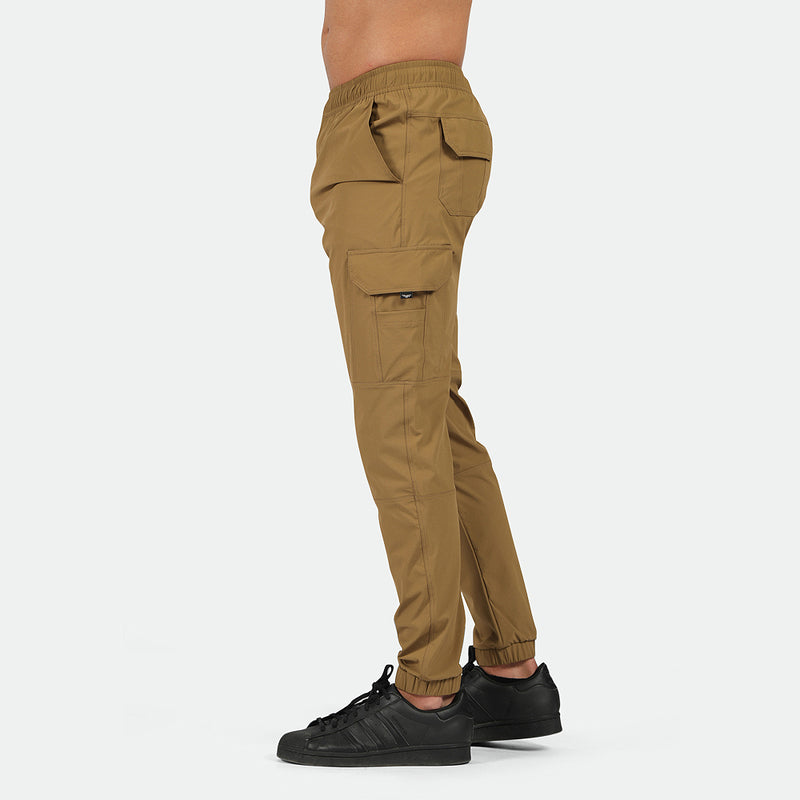 a fit man stand at right and wearing  pants cargo Breen brown with shoes black 