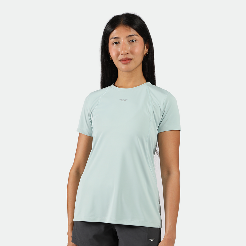 a fit woman look at the camera and smile ,she wearing t-shirt PASTEL-BLUE with short grey ,plus the background is light grey 