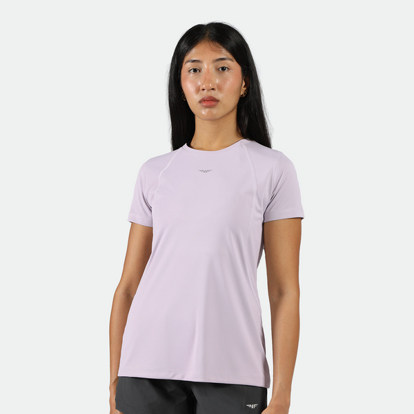  a fit woman look at the camera 
 and wearing a light purple athletic t-shirt, black shorts, plus the background is light grey 