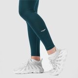 a fit woman  stand  at right and wearing  legging green with logo ,she wearing shoes white, plus the background is light grey  
