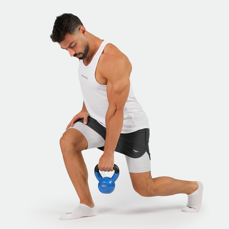 Man in white tank top and black shorts performs a lunge exercise, holding a blue kettlebell. He looks focused, set against a plain white background.