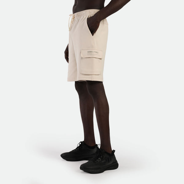 a fit man stand at right and wearing short beige with  pocket and logo plus shoes black 