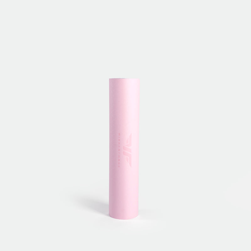 A tall, cylindrical, pastel pink yoga mat against a plain white background. The minimal design conveys simplicity and elegance, with a subtle logo.