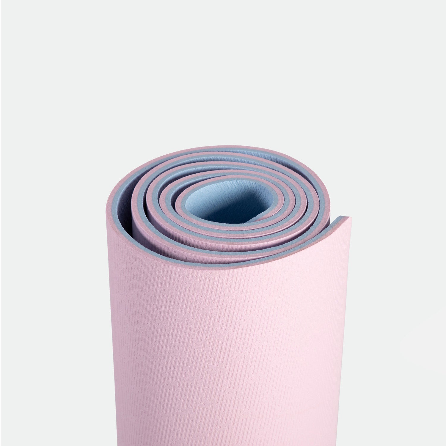 A rolled yoga mat with a pink exterior and blue interior on a white background, conveying a sense of calm and readiness for fitness or relaxation.