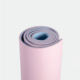 A rolled yoga mat with a pink exterior and blue interior on a white background, conveying a sense of calm and readiness for fitness or relaxation.