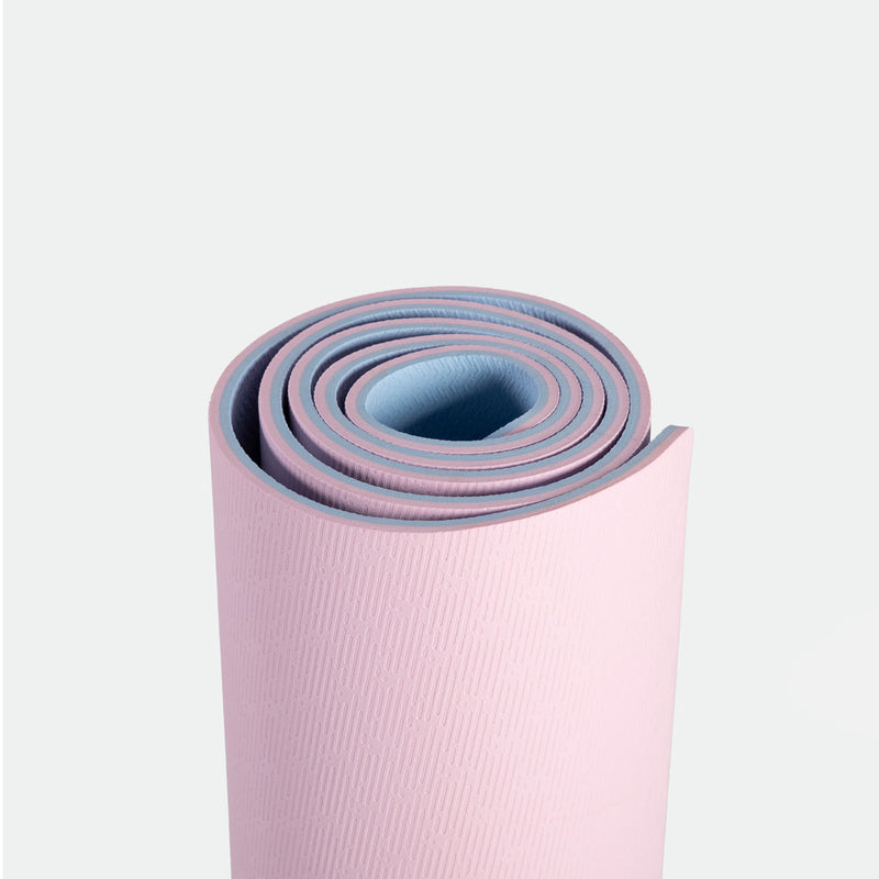 A rolled yoga mat with a pink exterior and blue interior on a white background, conveying a sense of calm and readiness for fitness or relaxation.