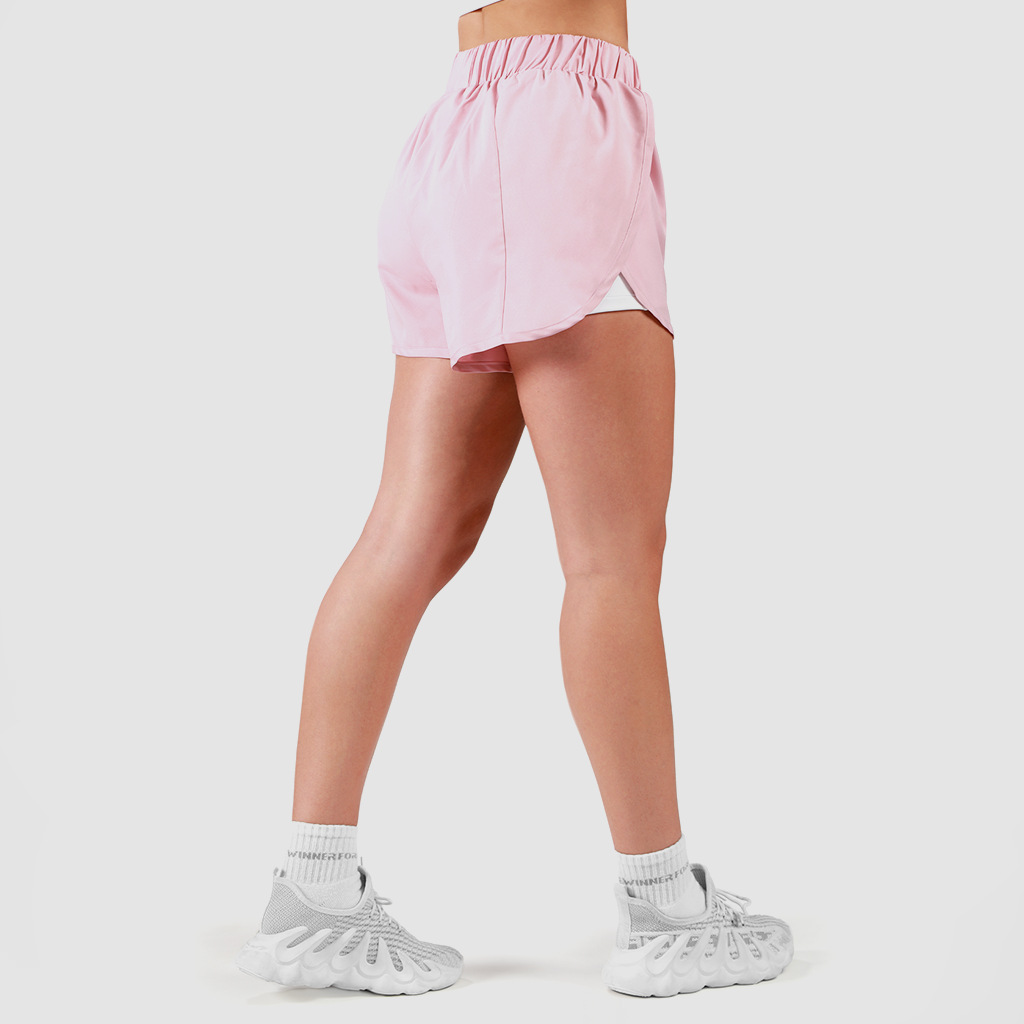 a fit woman stand at right and wearing pink short pink 2 in 1 with shoes white  plus the background is light grey 