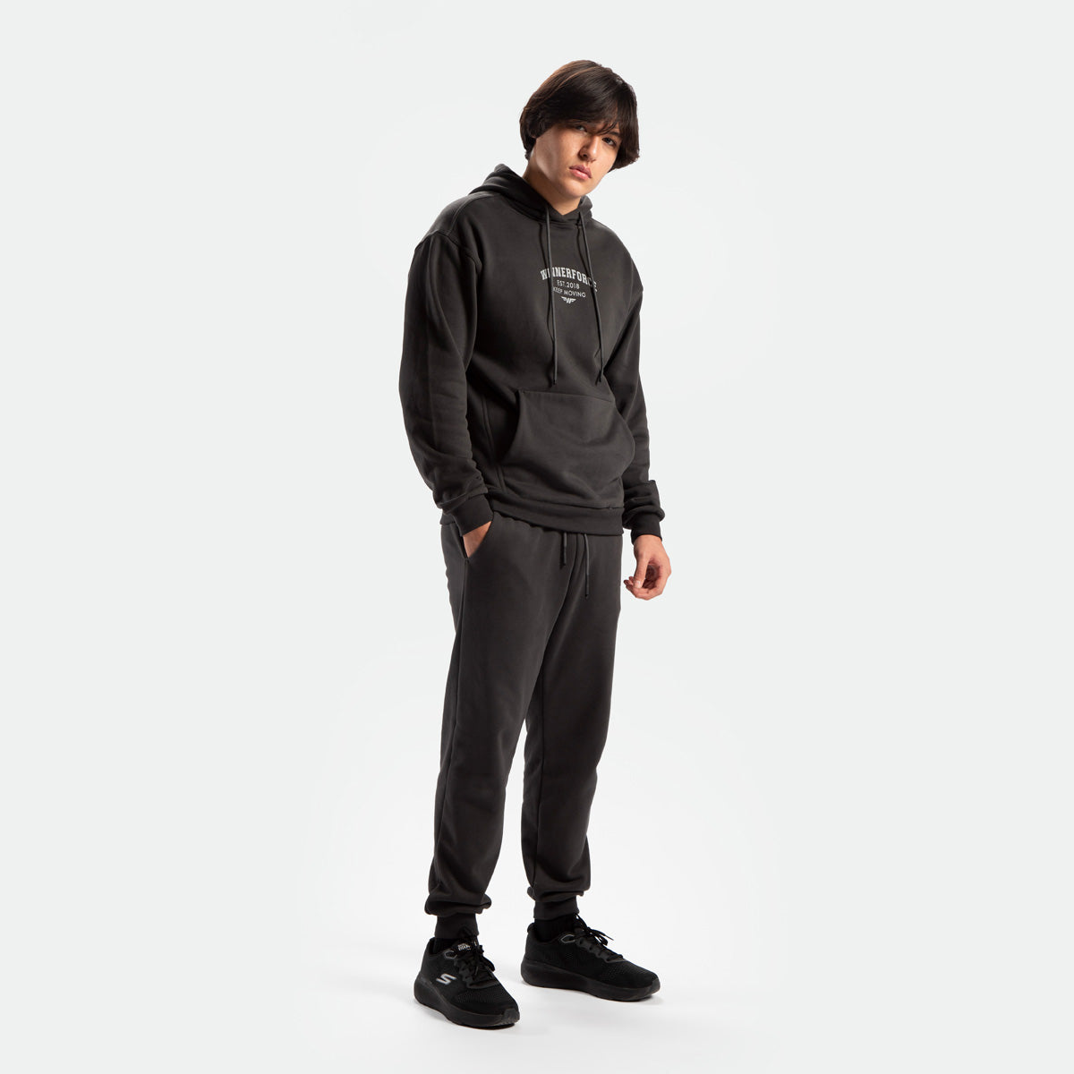 a fit man stand at right and wearing matching set pirate black ,hoodie and pants ,plus shoes black 